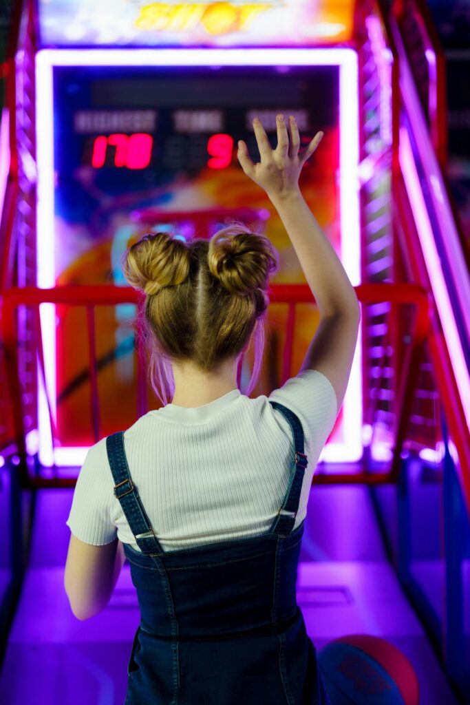 Young woman enjoying an arcade basketball game indoors with vibrant neon lights.