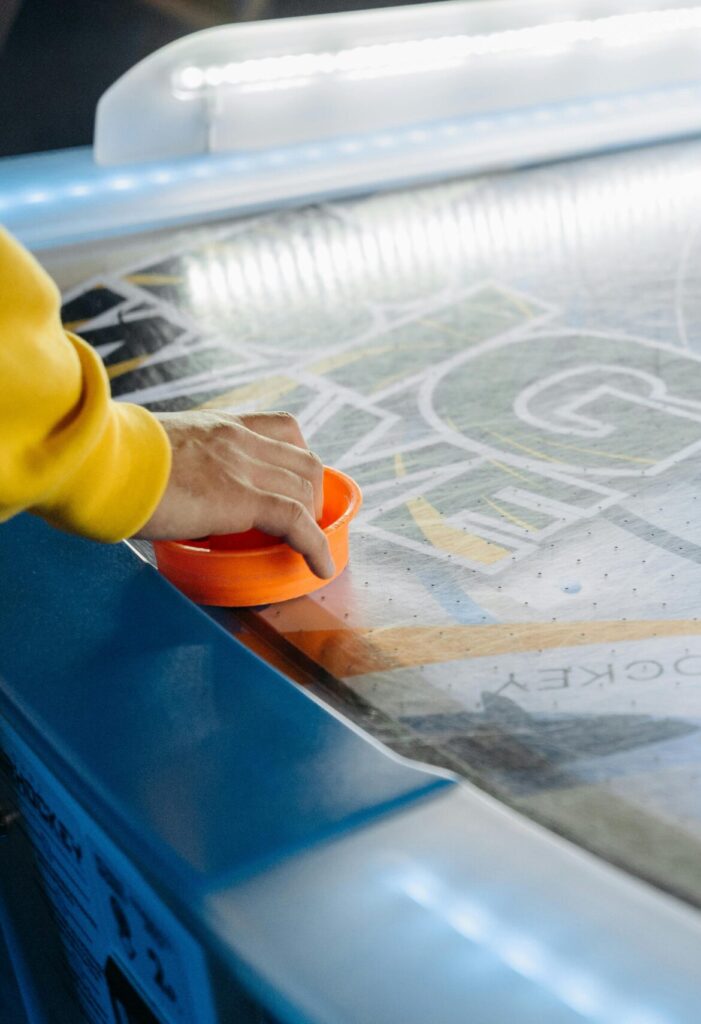 A person playing air hockey, focusing on hand, puck, and table during a game indoors.